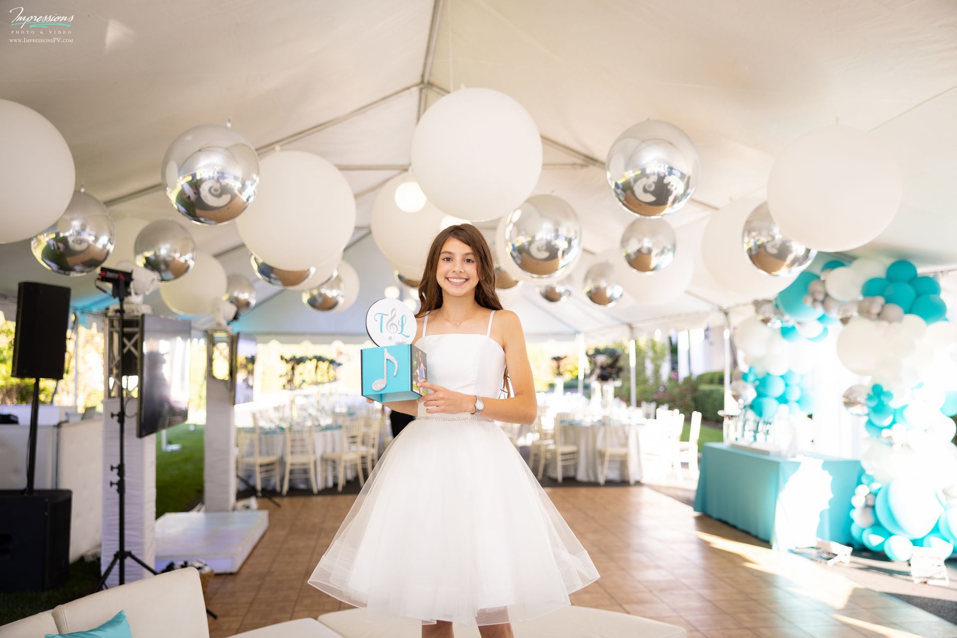Tent Ceiling Treatment with Large White Balloons andMetallic Silver Orbz, Beautiful White and Turquoise Organic Balloon Wall and Bat Mitzvah Girl Holding her Custom Logo & Picture Cube for Cocktail Centerpiece